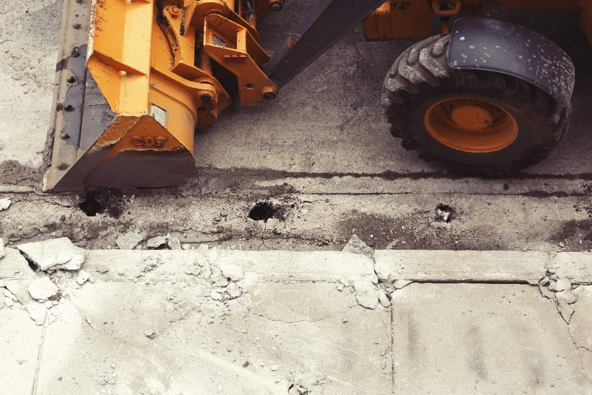 picture of a tractor next to a road that needs construction work illustrating the need for road base material suppliers in Southern California.