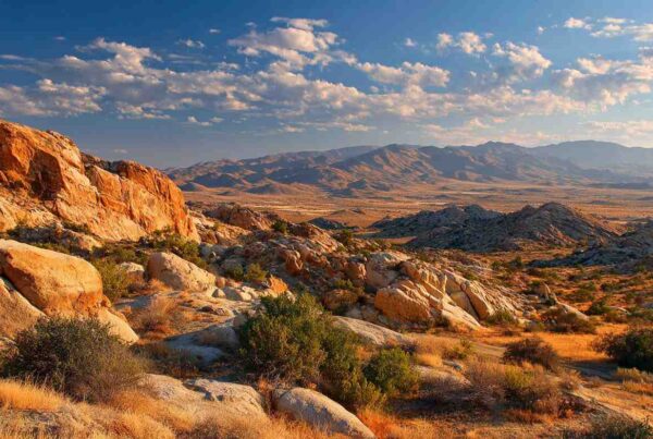 A vast desert landscape with rugged rock formations and sunlit terrain, showcasing the natural beauty of a high desert rock quarry environment.