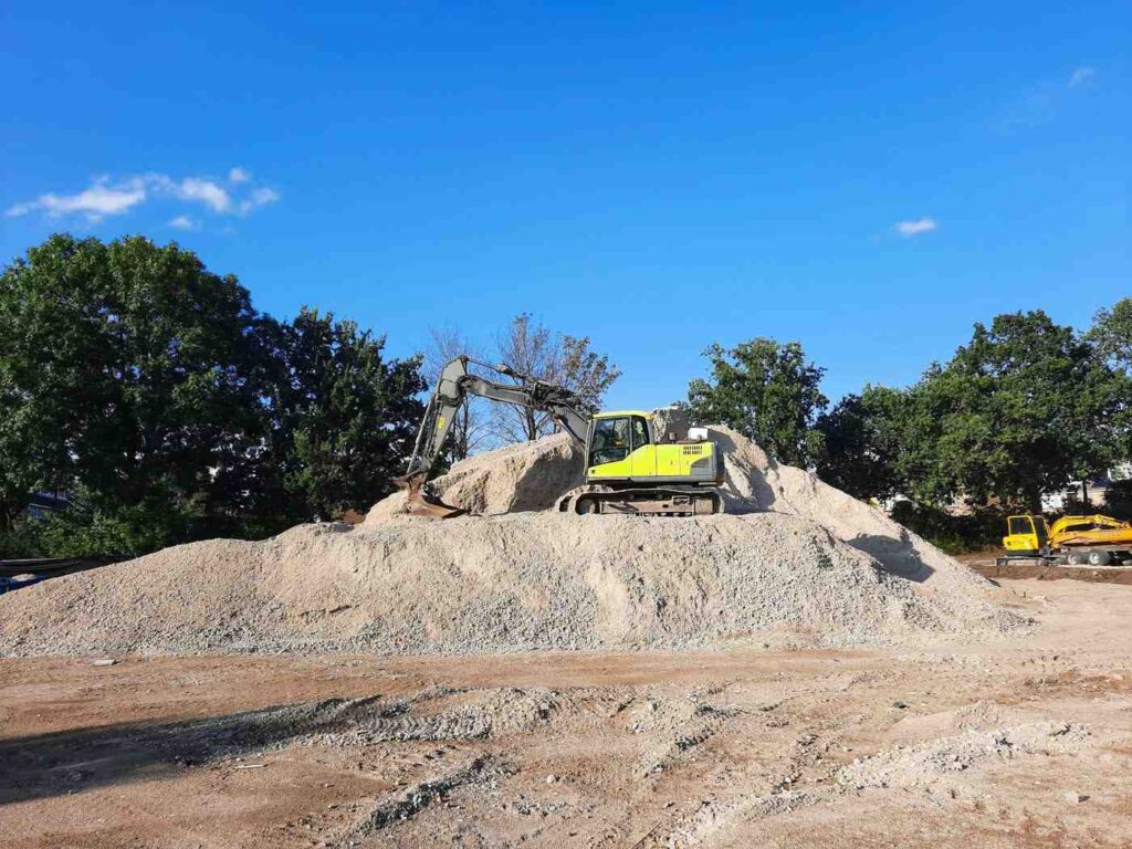 A yellow excavator works atop a pile of gravel and dirt, highlighting aggregate and fill dirt road construction.