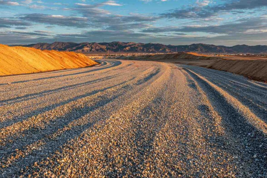 A newly prepared gravel road curves through a construction site, showcasing aggregate and fill dirt road construction.