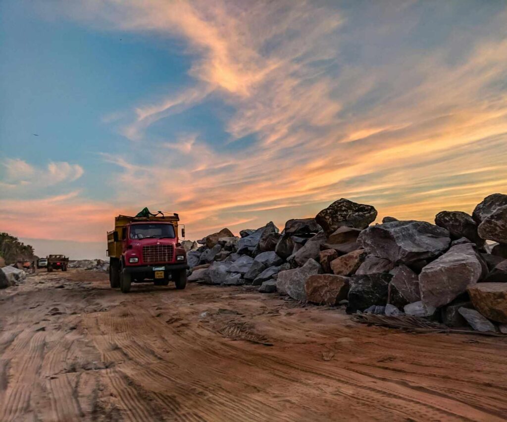 A red dump truck driving past large granite rocks at sunset, representing bulk granite supply.